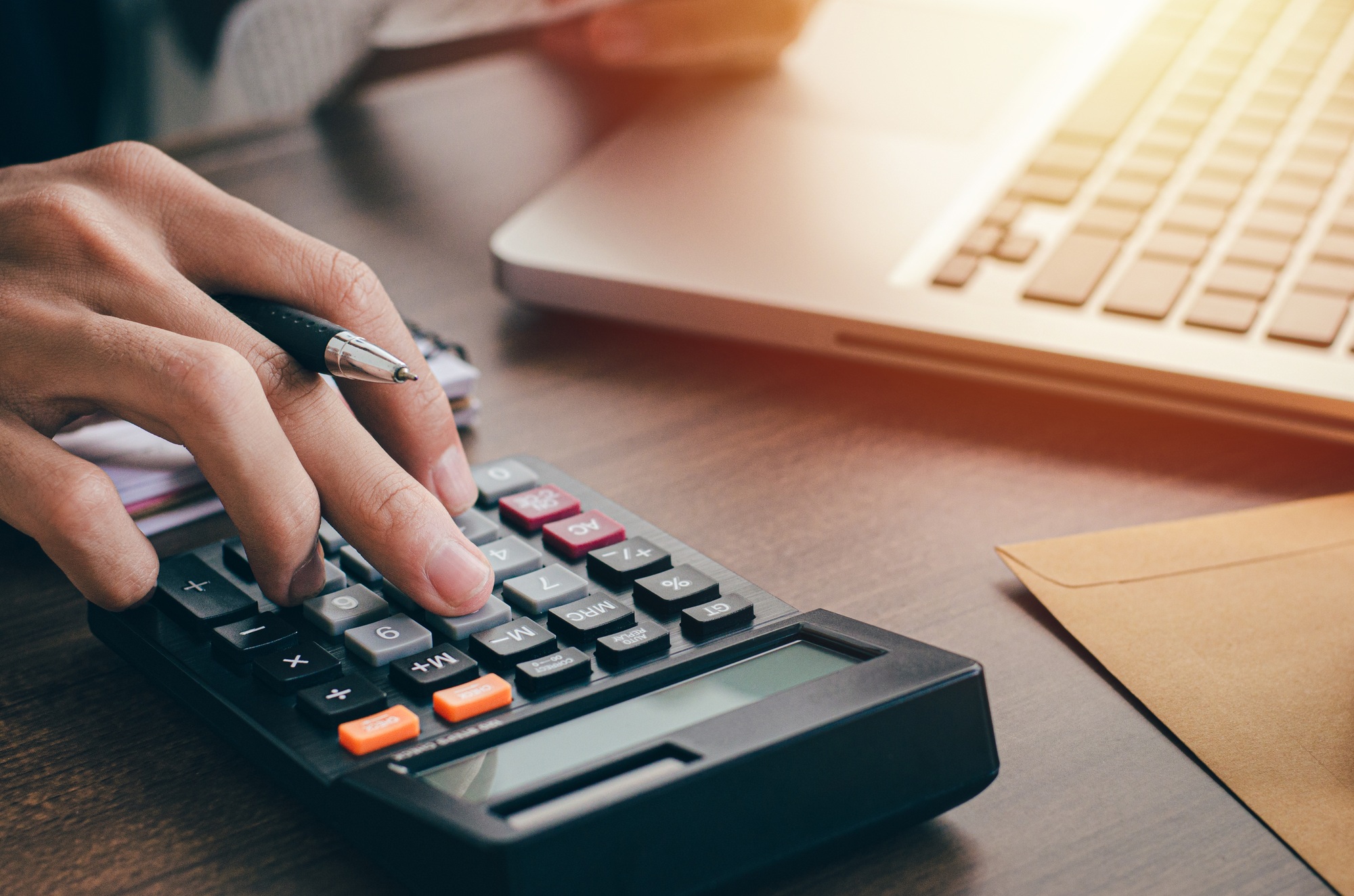 Young male investor calculating investment costs with a calculator and holding banknotes in hand.